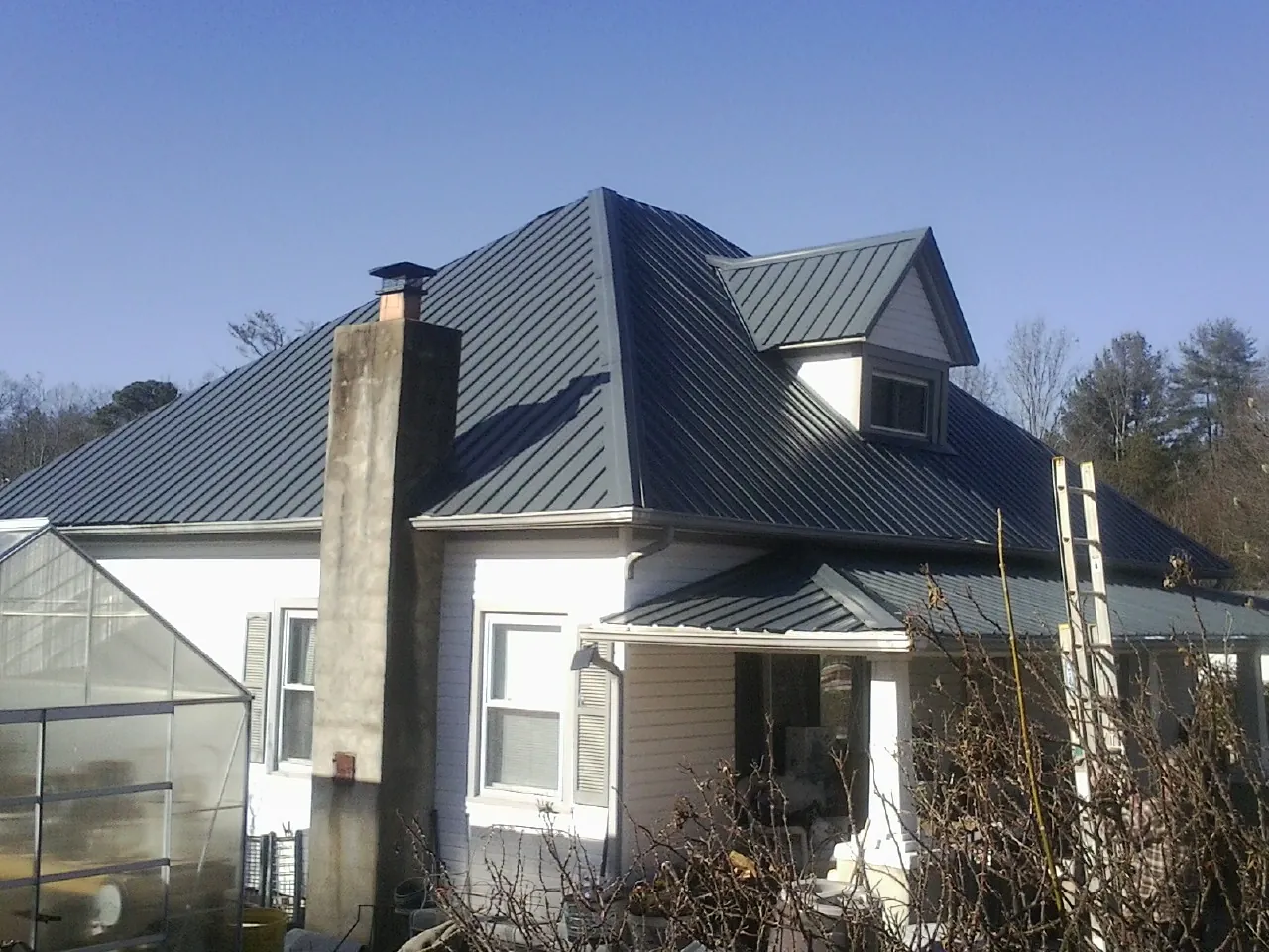 Dark blue standing seam metal roof on a white farmhouse with dormer — Slate & Tile Roof Repair by Roofing Brothers in Kootenai
