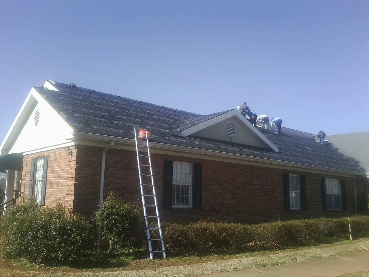 Crew tearing shingles off a brick ranch roof with a ladder set — Emergency Roof Repair work by our crew in Kootenai