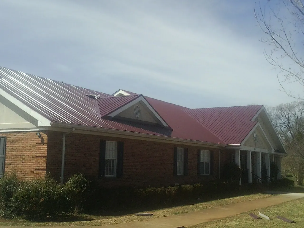 Red metal roof with gabled entries on a long brick building, from a Hail Damage Roof Repair job in Kootenai