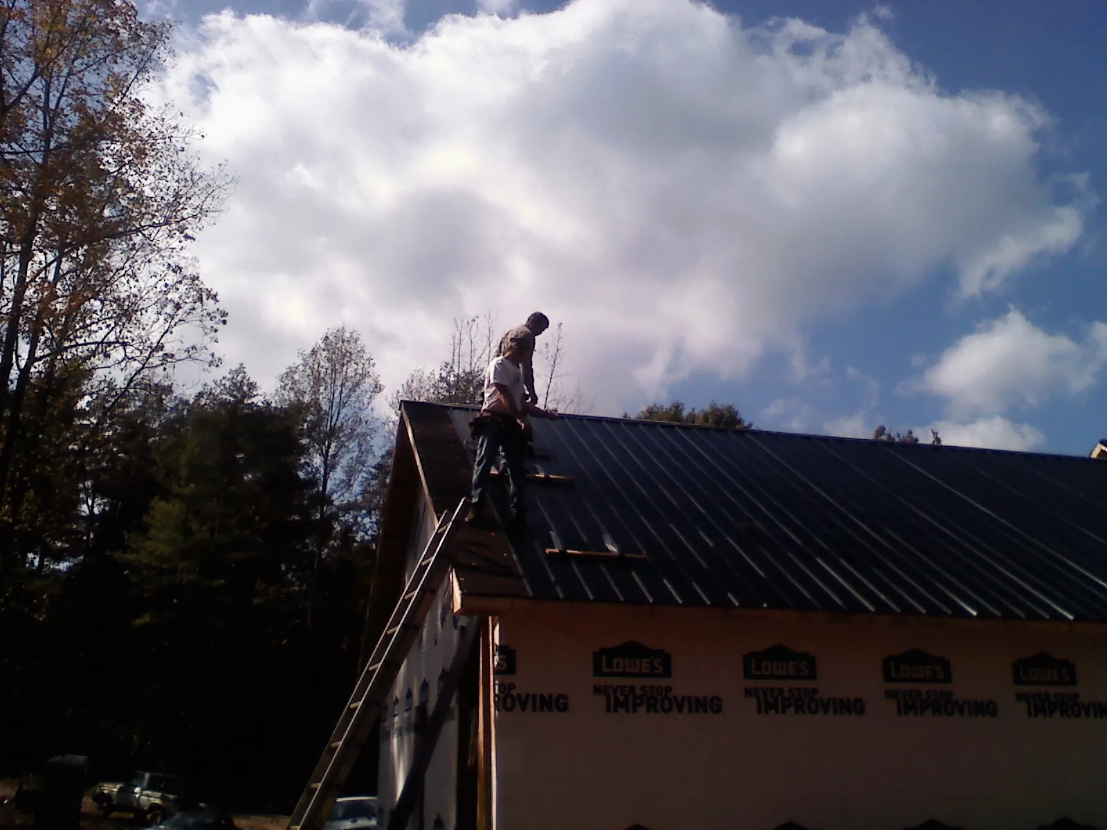 Roofer fastening dark metal panels high against a cloudy sky, from a Roof Inspection job in Kootenai
