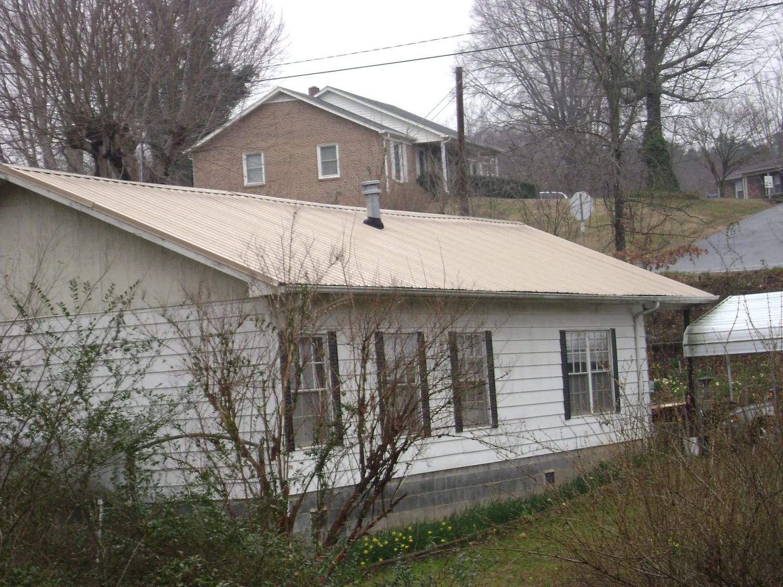 Tan metal roof on a white sided house set into a hillside — Commercial Roofing by Roofing Brothers in Kootenai